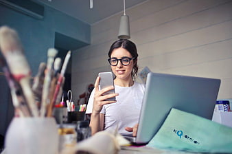 Woman artist using smartphone and laptop in creative workspace