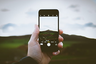 Hand holding smartphone taking photo of green highland landscape