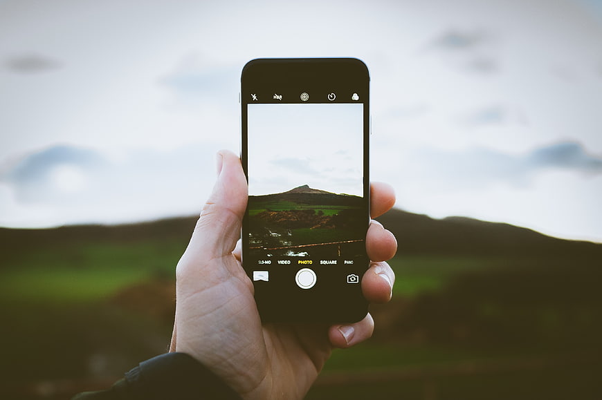 Hand holding smartphone taking photo of green highland landscape