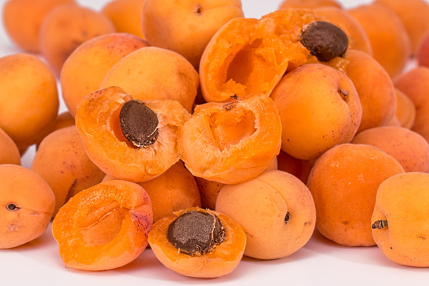 Fresh ripe apricots with cut halves and pits on white background