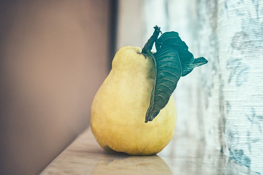 Close-up of a yellow pear with green leaves on a wooden surface