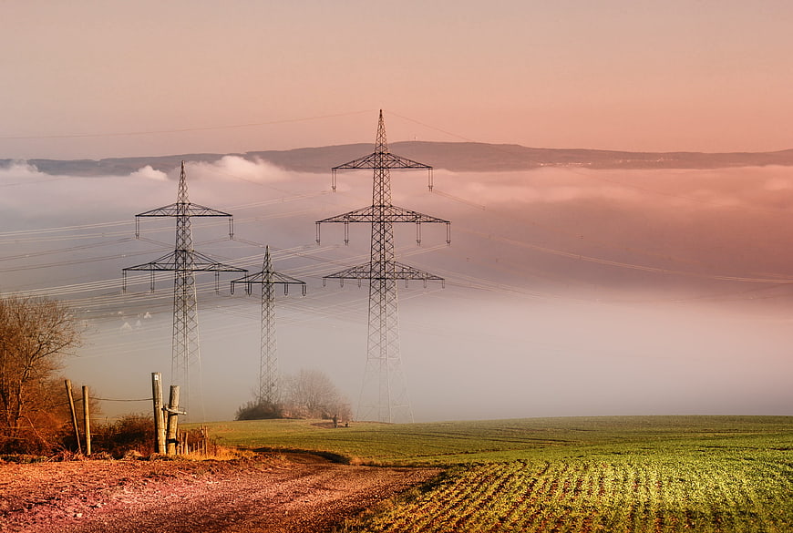 Electricity Pylons in Foggy Green Field at Sunrise