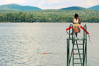Lifeguard woman sitting on tower overlooking lake and mountains