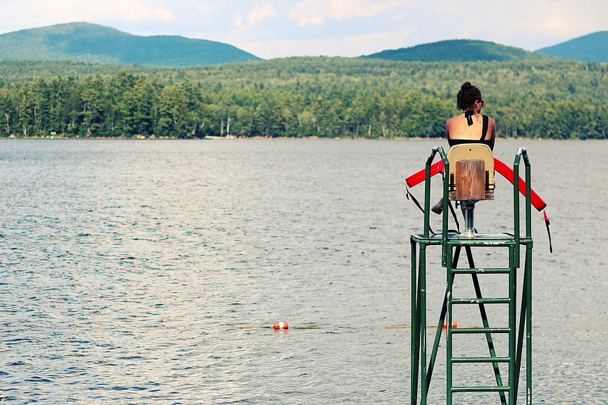 Lifeguard woman sitting on tower overlooking lake and mountains