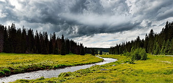 Winding River Through Green Meadow Under Stormy Sky