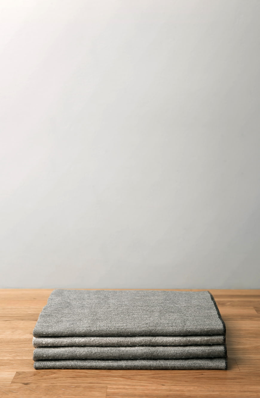 Stack of folded gray towels on wooden table with white background