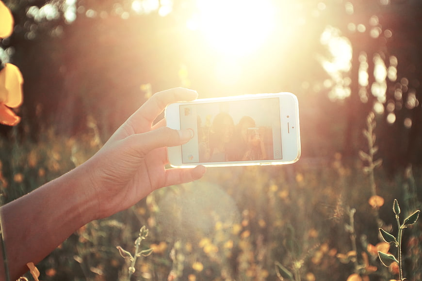Hand holding smartphone taking selfie in sunny field