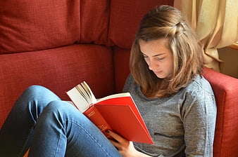 Young woman reading a red book on a red sofa