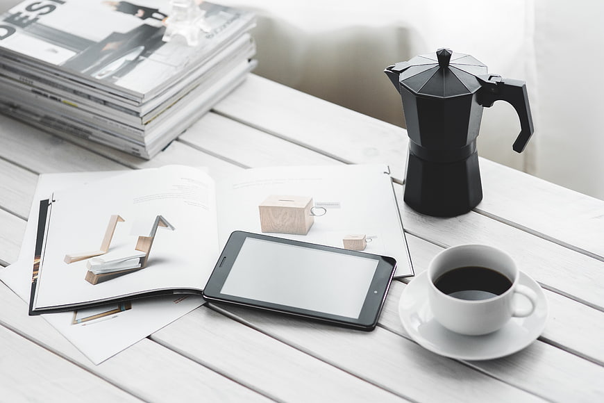 Modern workspace with tablet, coffee, and magazines on white desk