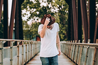 Man in Fedora Tipping Hat on Rustic Bridge