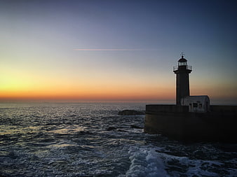 Lighthouse on rocky coast at sunset with ocean waves