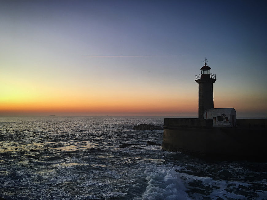 Lighthouse on rocky coast at sunset with ocean waves