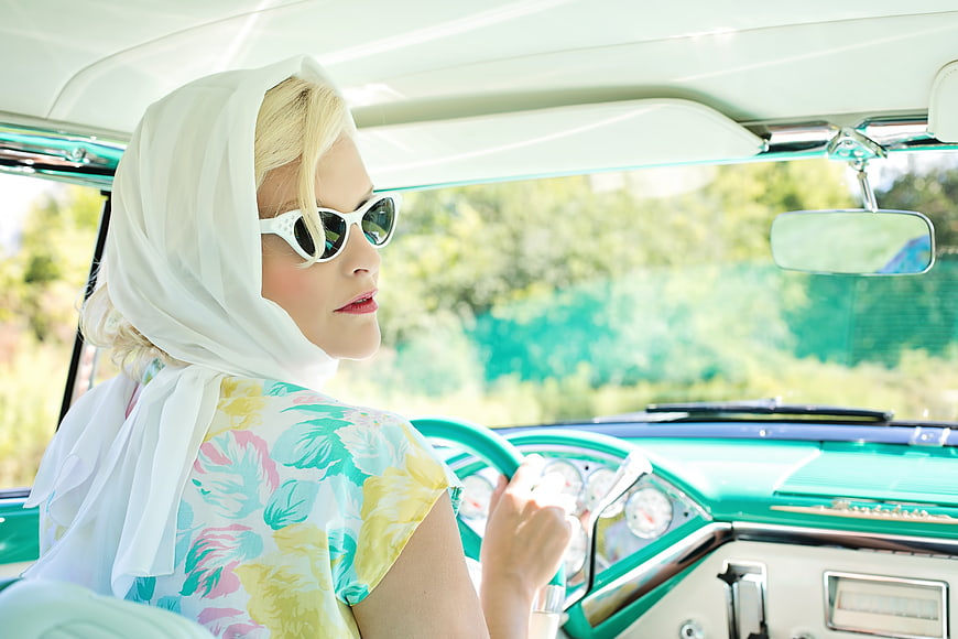 Blonde woman in vintage car with headscarf and sunglasses