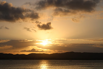Golden sunset over ocean with silhouetted hills and clouds