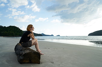 Woman sitting on log looking at ocean beach