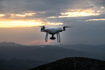 White drone flying over mountains at sunset