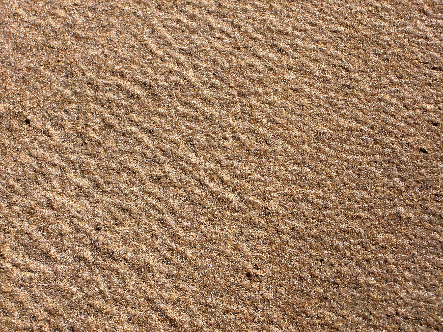 Close-up of wet sand texture with natural ripples and granular detail