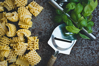 Top view of rigatoni pasta, basil, and grater on rustic background