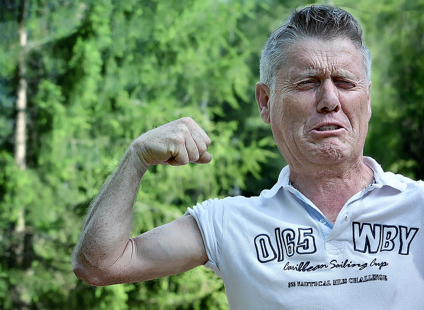 Senior man flexing bicep with effort outdoors