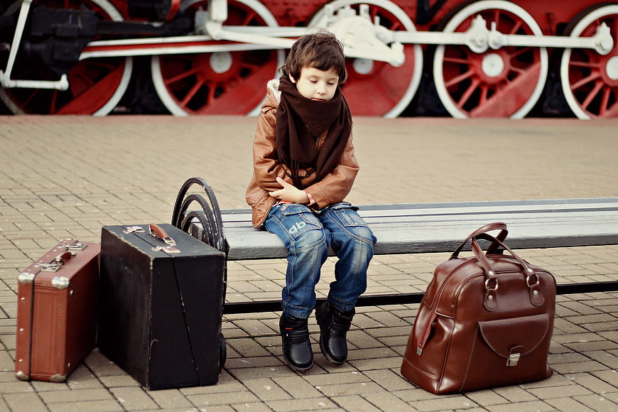 Sad boy waiting with vintage suitcases at train station