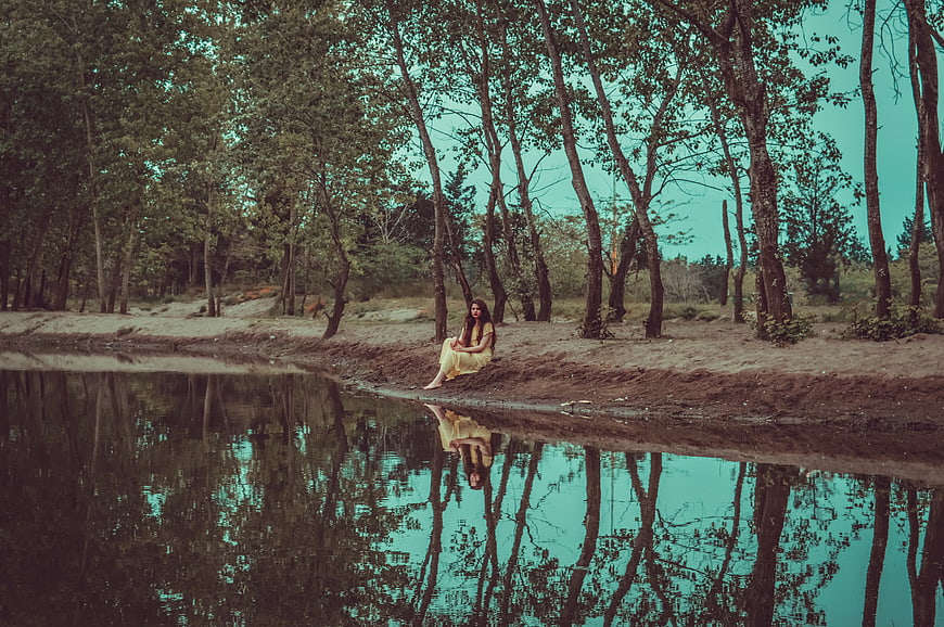 Woman in Yellow Dress Sitting by Lake with Reflection