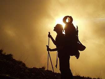 Silhouette of hiker with backpack and poles against golden sunset