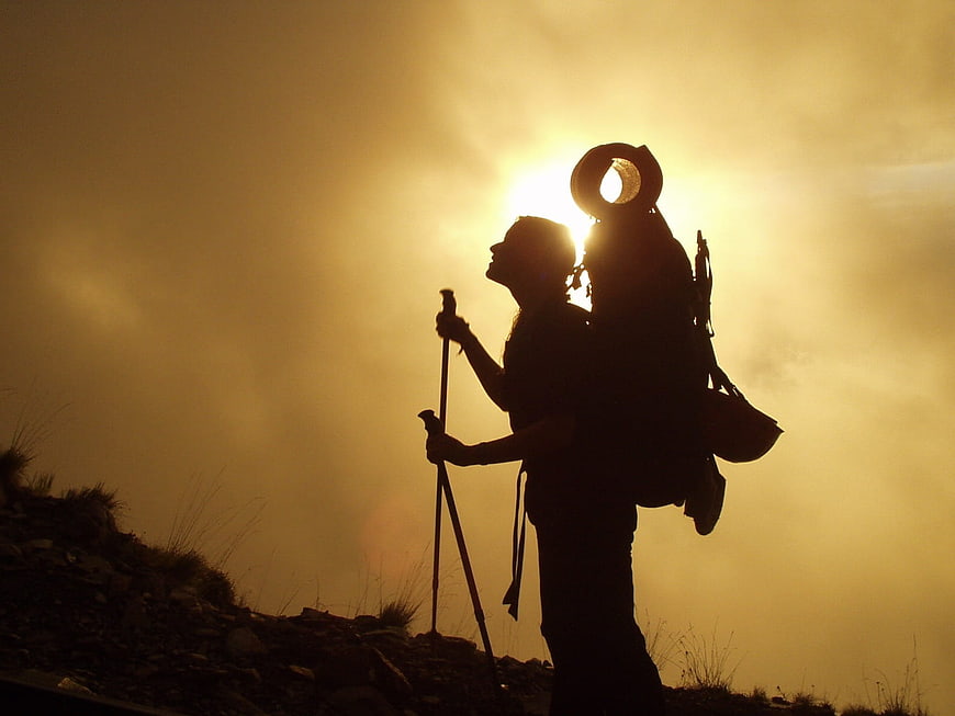 Silhouette of hiker with backpack and poles against golden sunset