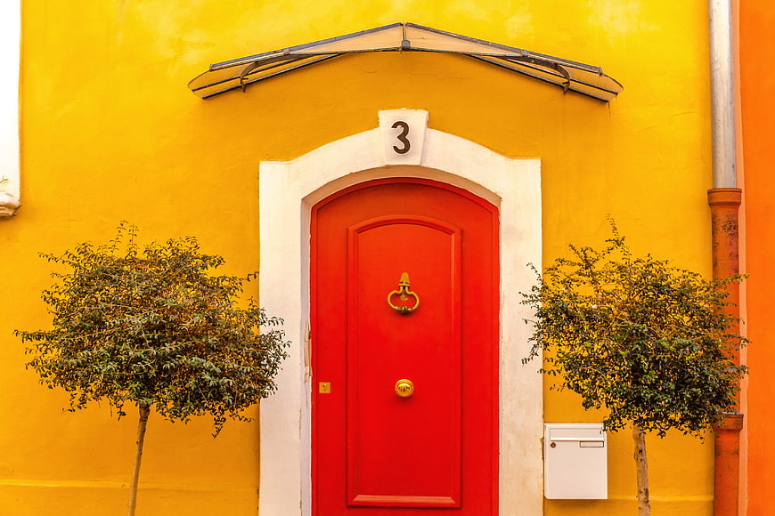 Vibrant Red Door on Yellow Wall with Symmetrical Bushes