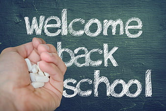 Hand holding white pills with welcome back to school text on chalkboard