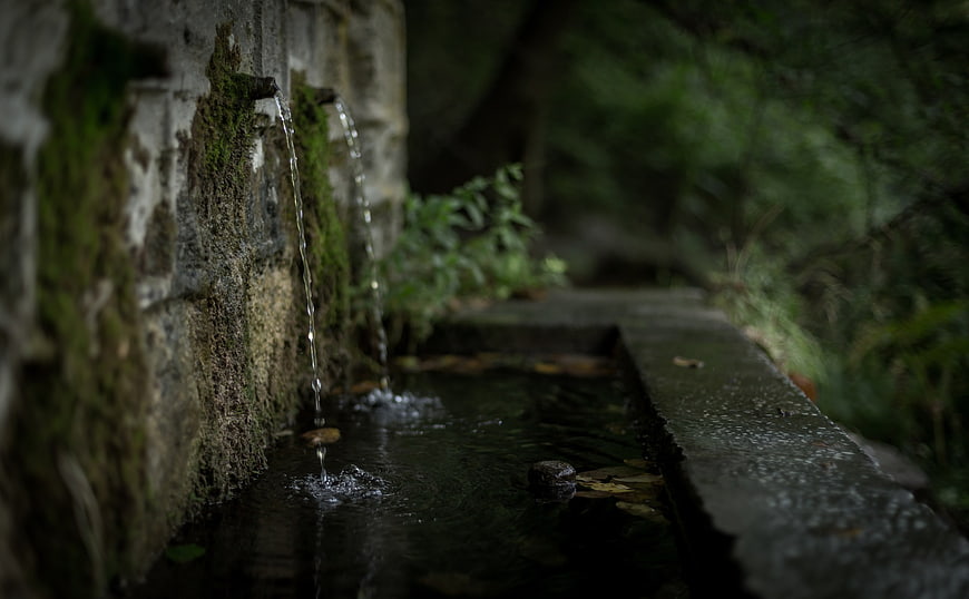 Mossy stone fountain with flowing water in a dark forest