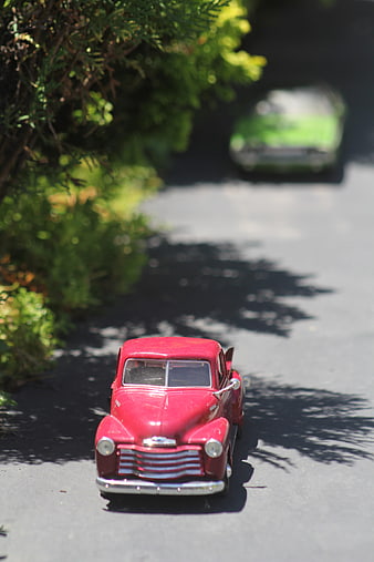 Red vintage toy truck on asphalt road with greenery