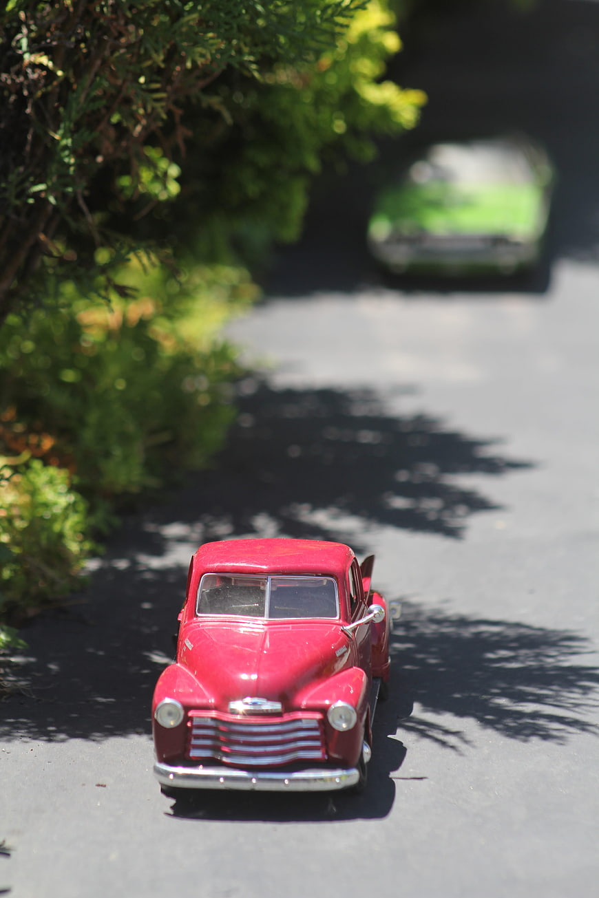 Red vintage toy truck on asphalt road with greenery