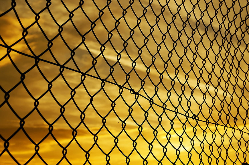 Chain link fence silhouette against golden sunset sky
