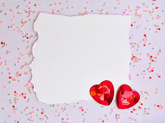 White paper with red heart gems and confetti flat lay