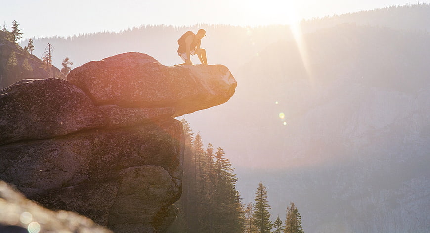 Hiker sitting on rocky cliff edge at sunrise