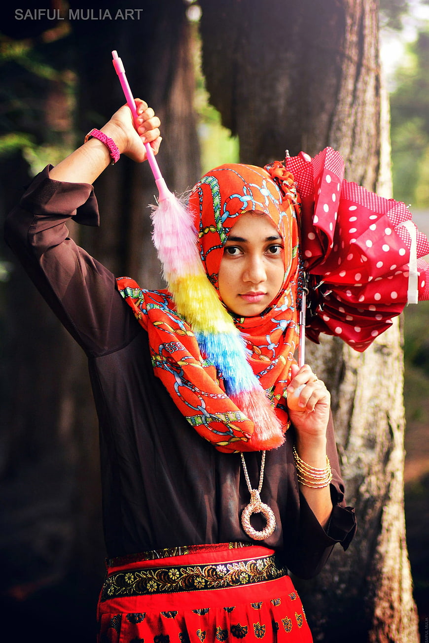 Young woman in traditional Indonesian batik attire holding colorful feathered prop