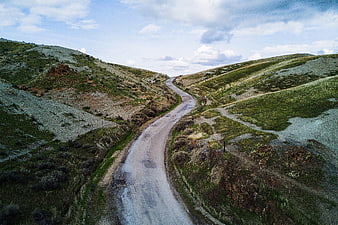 Winding dirt road through green hills under cloudy sky