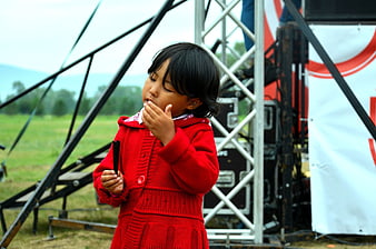 Little girl in red coat eating outdoors near stage