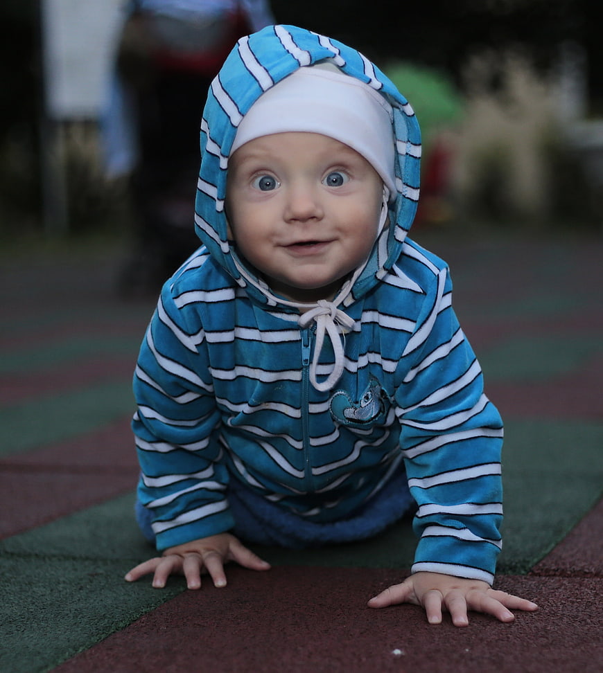 Baby boy in blue striped hood crawling on playground surface
