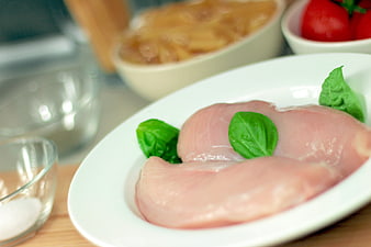 Raw chicken breasts with basil on white plate