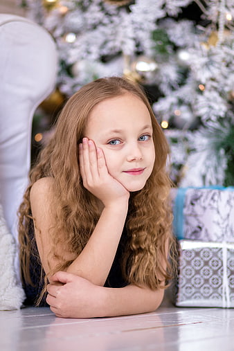 Cute girl with curly hair resting chin on hand near Christmas gifts