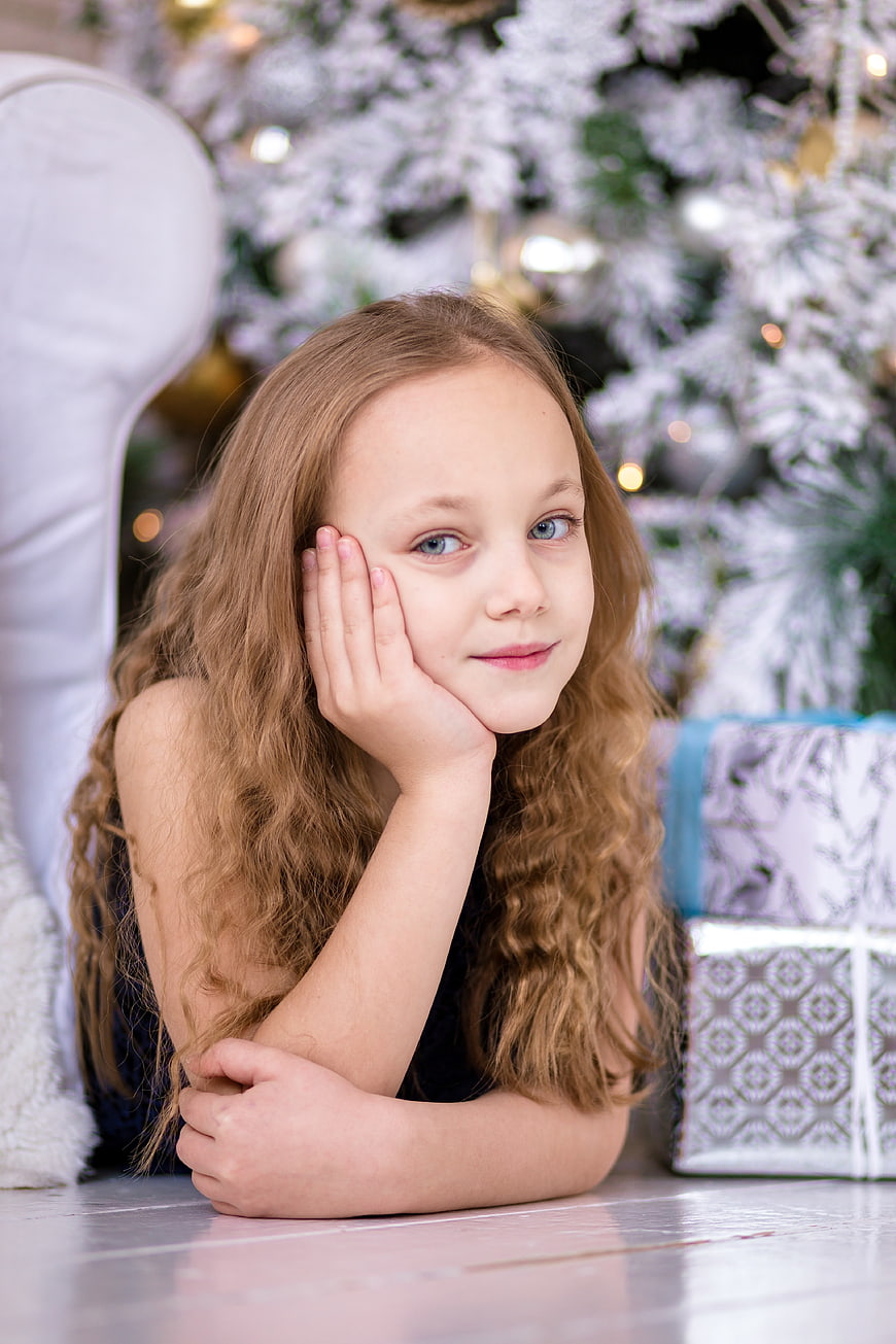 Cute girl with curly hair resting chin on hand near Christmas gifts