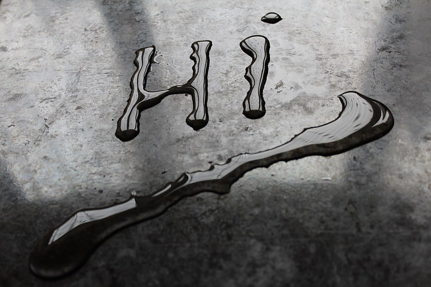 Water Droplets Forming The Word Hi On Textured Concrete Surface
