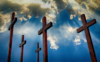 Five wooden crosses against dramatic blue sky with sun rays