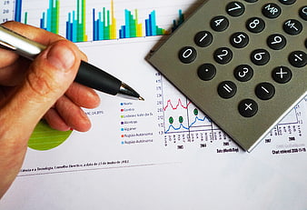 Hand with pen analyzing financial charts and calculator