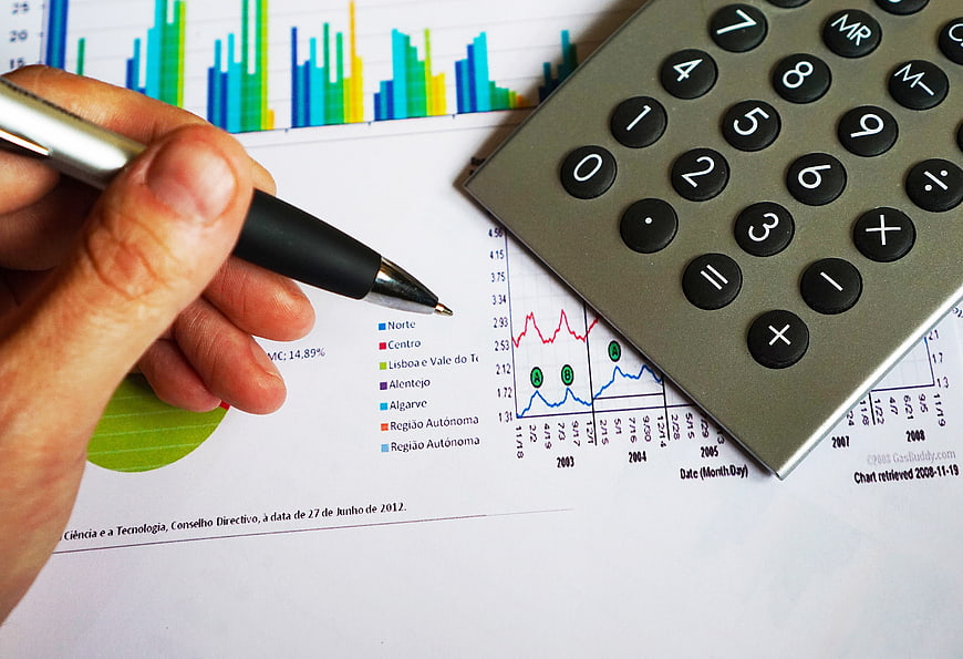 Hand with pen analyzing financial charts and calculator