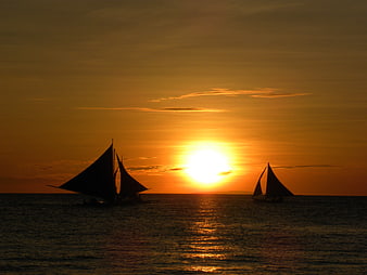 Silhouetted traditional dhows sailing at golden sunset