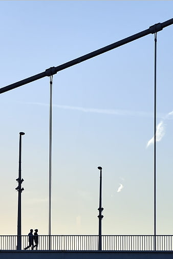 Silhouette of Couple Walking on Suspension Bridge Against Blue Sky