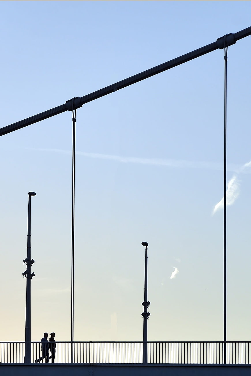 Silhouette of Couple Walking on Suspension Bridge Against Blue Sky
