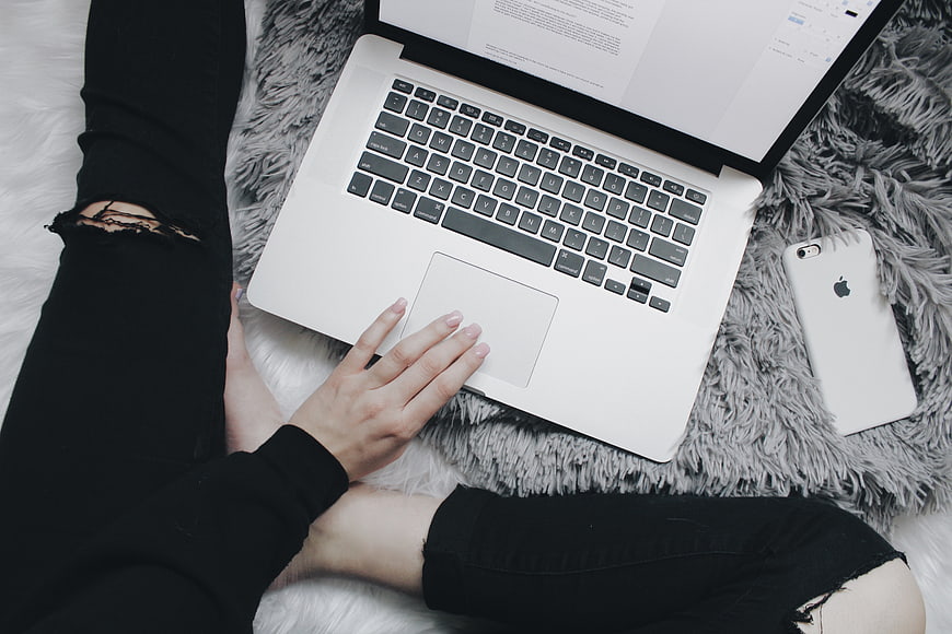 Woman using laptop on fluffy rug with smartphone